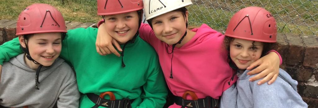 Four girls sitting at climbing wall in helmets.