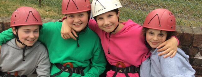 Four girls sitting at climbing wall in helmets.